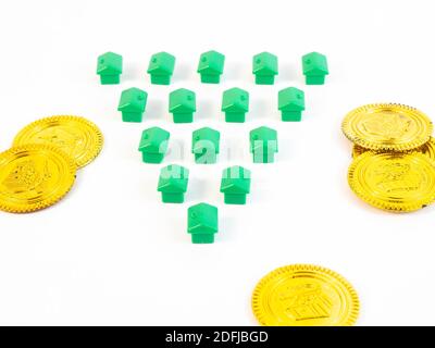 Green colored pawns in the shape of a house with gold coins. Concept around housing and real estate agents. Stock Photo