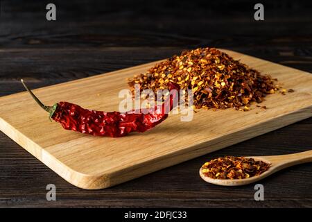 Red hot chilli pepper dry pod and flakes on a cutting board over black wood table. Natural spices and seasonings for meat, fish and vegetable dishes. Stock Photo