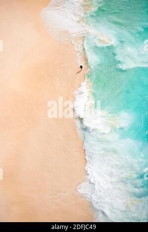 View from above, stunning aerial view of an unidentified person walking on a beautiful beach bathed by a turquoise sea. Kelingking beach, Nusa Penida.
