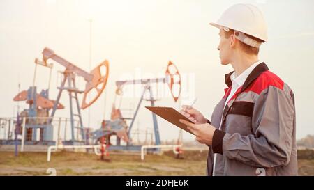 engineer writing on clipboard in oil field. Industrial, oil and gas concept. Stock Photo