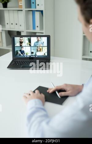 Several young colleagues on laptop display looking at businessman sitting by desk in office during online communication through video chat Stock Photo