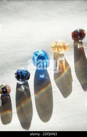 Row of glass beads of various colors, sizes and shapes for necklaces and their long shadows on wooden table painted in white Stock Photo
