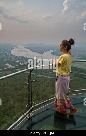 Skywalk, overlooking Sangkhom, and Mekong River Thai woman in traditional dress looking out from high viewpoint over the countryside below