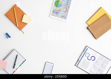 Top view of supplies of office worker or broker - financial papers in clipboard, notebooks, gadgets, notepaper, stapler surrounding copyspace Stock Photo