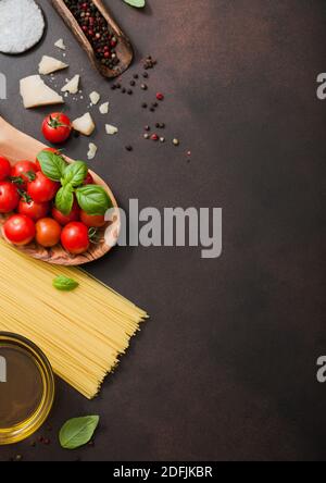 Spaghetti with tomatoes in wooden bowl with oil and parmesan cheese with salt on dark brown background. Top view Stock Photo