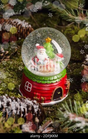 A cute Christmas toy, a snow globe with Santa Claus, a snowman and a Christmas tree inside. Christmas gift and decor idea Stock Photo