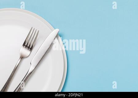 White ceramic plate and cutlery on a blue background with copy space. Food background. Stock Photo