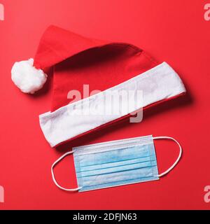 Rolled up Santa Claus hat and disposable medical mask on a red background, top view. Concept on the theme of quarantine during the Christmas holidays Stock Photo