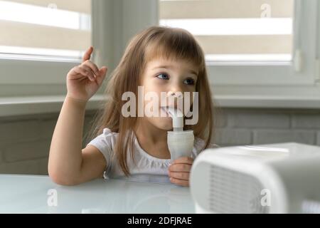 beautiful little girl uses a nebulizer at home. treatment of bronchitis and asthma with inhalation Stock Photo