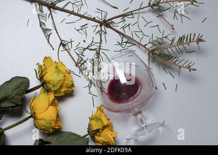 A bouquet of dried yellow roses. An overturned glass with sour wine and a spruce branch with fallen heads. On pine boards. Stock Photo