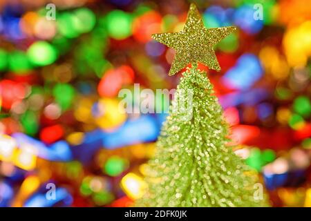 Small toy fir tree with star against defocused christmas decoration. Selective focus on the star Stock Photo