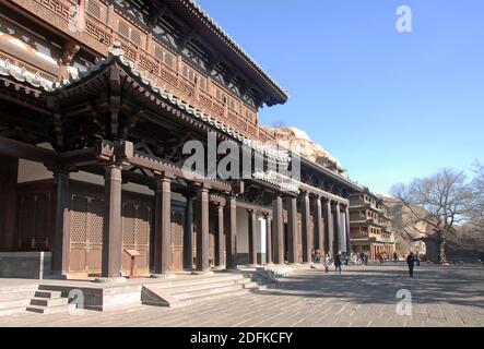 Yungang Grottoes near Datong, China. Exterior view of the grottoes with visitors. The wooden buildings are attached to the cliff in front of the caves Stock Photo