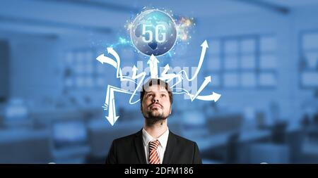 businessman with a virtual world map with message 5G over his head in front of an office background Stock Photo