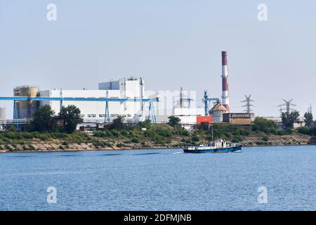 industrial landscape with a factory on the banks of the river, along which a tugboat floats Stock Photo