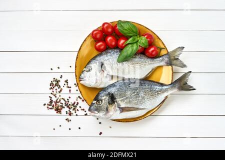 Raw fresh dorado fish on yellow plate and vegetables on white table. Top view copy space Stock Photo
