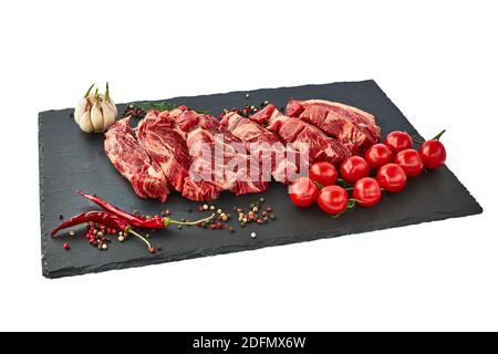 Fresh raw beef steaks with pepper and tomatoes on a black slate board. Isolated over white Stock Photo