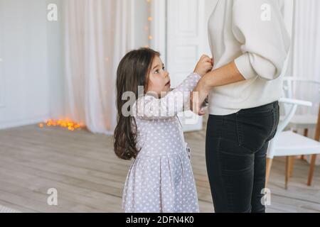 Cute long hair little girl helps dress her mother at bright bed room Stock Photo