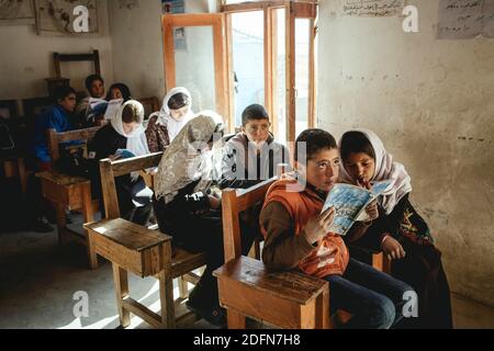 Nine students in classrooms, a boy and a girl reading in the first bank, Potokh Primary School, Potokh, Wakhan Corridor, Afghanistan Stock Photo