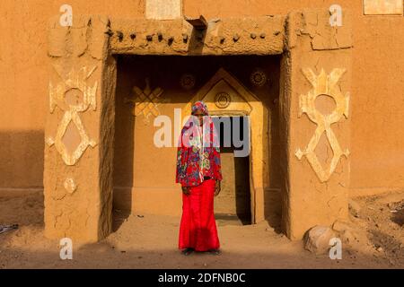 Young girl in traditional clothing in front of a mud house, Agadez, Niger Stock Photo