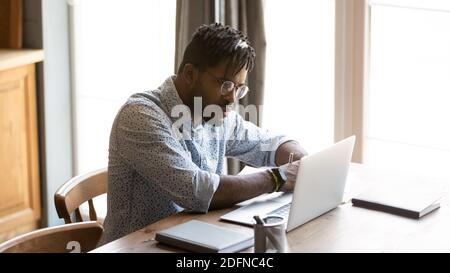 Focused young african american man watching educational webinar on laptop. Stock Photo