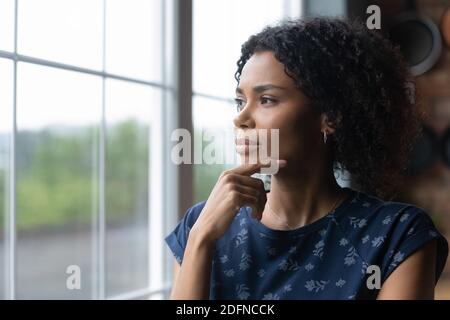Thoughtful millennial african american woman standing near window.