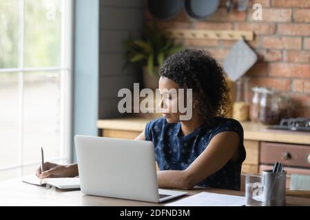 Focused young african american woman writing notes, working on computer. Stock Photo