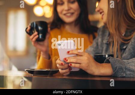 Two female friends meeting at a coffee shop. Woman holding mobile phone sitting with a friend at cafe. Stock Photo