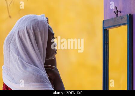 African Ghana woman standing in front of a mirror with a white shawl covering her hair Stock Photo