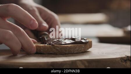 man spreading chocolate hazelnut spread on ciabatta slice on wood board, wide photo Stock Photo