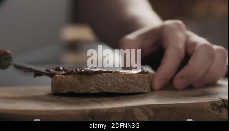 man spreading chocolate hazelnut spread on ciabatta slice on wood board, wide photo Stock Photo