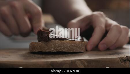 man spreading chocolate hazelnut spread on ciabatta slice on wood board, wide photo Stock Photo