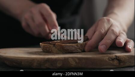 man spreading chocolate hazelnut spread on ciabatta slice on wood board, wide photo Stock Photo