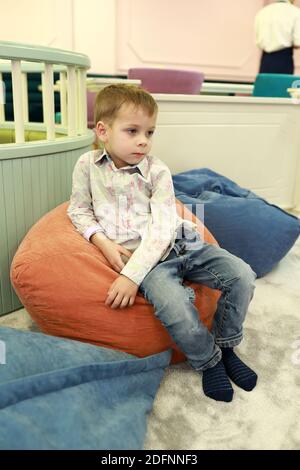 Pensive child sitting on bean bag chair Stock Photo