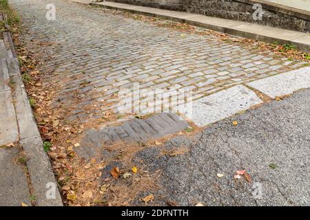 Roadway of mixed asphalt and grey stones, patchwork sidewalks and retaining wall, horizontal aspect Stock Photo