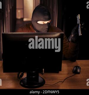Hacker in black balaclava with a printed circuit board from the device in hand. Concept of data security problems and network hacking Stock Photo