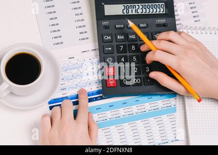 Calculator, a cup of coffee and papers with numbers. The man is counting on a calculator. Analytical report. Calculation of tax, income and expenses Stock Photo