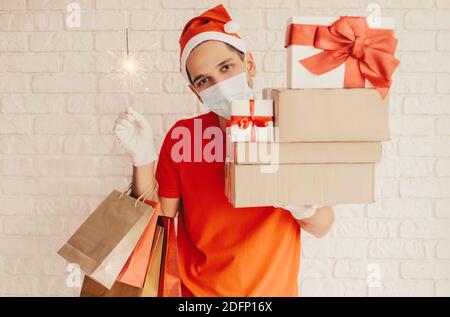 https://l450v.alamy.com/450v/2dfp16x/young-festive-delivery-man-in-medical-face-mask-protective-gloves-santa-hat-hold-light-sparkler-shopping-bags-cardboard-gift-boxes-and-smile-happ-2dfp16x.jpg