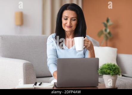 Mature woman holding coffe cup and working on computer Stock Photo
