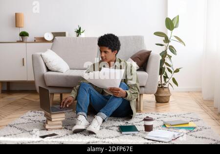 Young teen guy with educational materials, books and laptop computer working on cousework or school project at home Stock Photo
