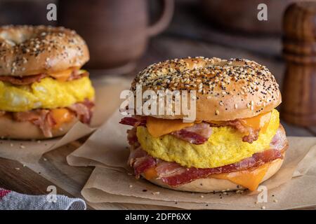 Bagel breakfast sandwich with bacon, egg and cheddar cheese on a rustic wooden table Stock Photo
