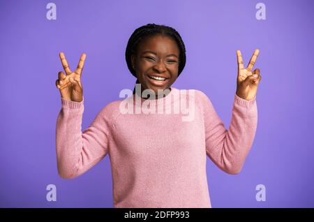 Peace. Joyful Black Young Woman Gesturing V-Sing And Laughing Over Purple Background Stock Photo