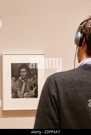 young man with headphones looks at photograph Dorothea Lange’s Migrant Mother  in Moma museum in New York City