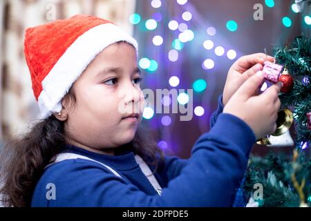 Girl in Santa cap decorating Christmas tree Stock Photo