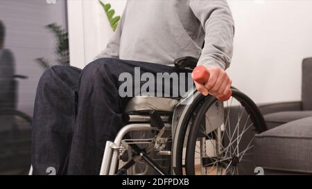 Man in wheelchair exercising and lifting weight in a living room. Stock Photo