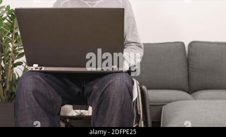 Young man in wheelchair with laptop working remotely from home, using internet and looking at screen. Stock Photo