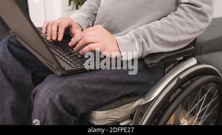 Young man in wheelchair with laptop working remotely from home, using internet and looking at screen. Stock Photo
