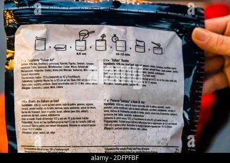 A traveler holds the packaging of the trekking meal "Balkan Art Rice Pan" with multilingual preparation instructions near Qalai Khumb, Tajikistan. Stock Photo