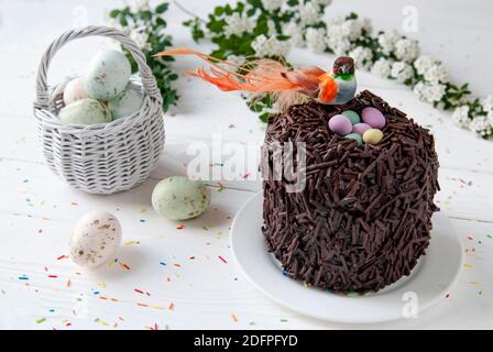 Easter chocolate cake and bird sitting in the nest. Little orange bird, colored eggs and wicker basket on a background of Easter’s décor Stock Photo
