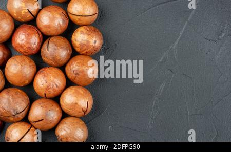 Scattered macadamia nuts in their shells on an empty dark background Stock Photo
