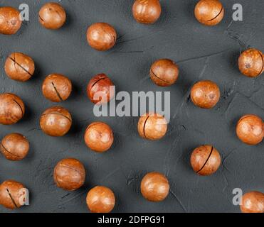 Scattered macadamia nuts in their shells on a dark concrete background, top view Stock Photo